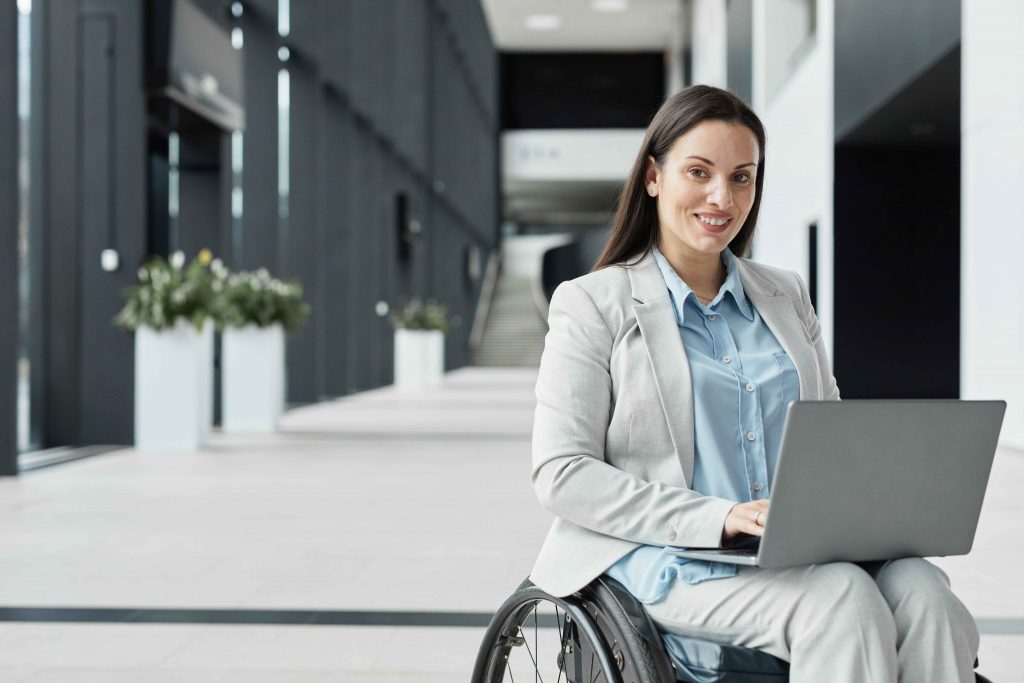 Travailleuse en situation de handicap dans un fauteuil roulant avec son ordinateur portable.